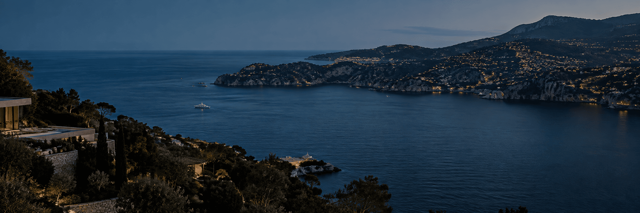 Aerial view of a rugged Mediterranean coastline at dusk with a yacht offshore